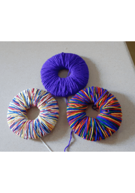 An animated image of three pompoms. The image quickly alternates between the pompoms wrapped around the card rings pre-cutting and the finished articles